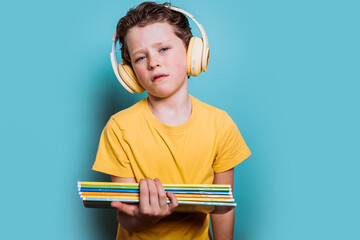 A school-aged boy in a yellow shirt holds a stack of books while wearing headphones, against a serene blue background