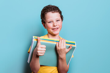 A young student in a yellow shirt gives a thumbs up while holding his school books, radiating positivity and readiness