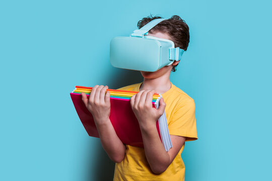 A schoolboy in a yellow shirt is engrossed in a virtual reality learning experience while holding textbooks