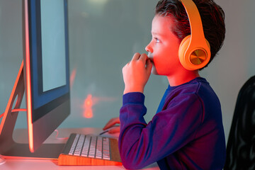 A focused child engages in gaming or interactive learning with headphones on at a computer with a vibrant backlight