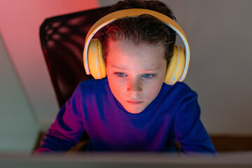 Intensely focused child with headphones using a computer, immersed in an online educational program or game