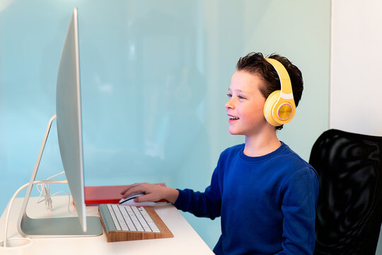 A cheerful child interacts with a computer, wearing bright yellow headphones, with a smile indicating enjoyment or success with the task at hand