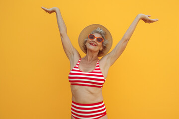 Cool funky elderly Latin American woman dressed striped red swimsuit dancing having fun isolated yellow color background