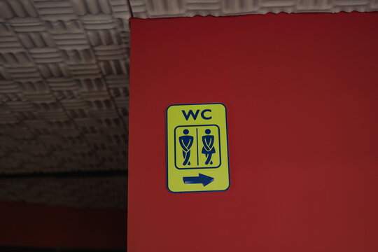 Restroom sign with directional arrow on red wall