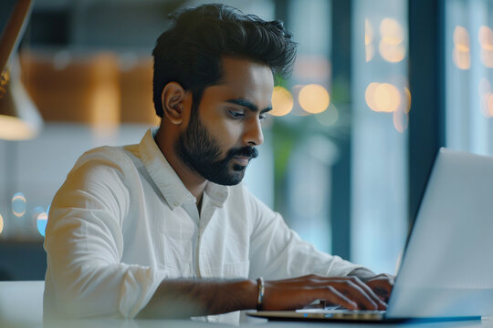 Focused Indian business man typing at laptop in office closeup. Guy surfing internet