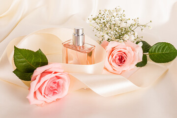 Chic bottle of women's perfume among beige satin ribbon, pink roses on fabric satin background....