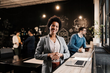 Portrait of a multicultural businesswoman with a laptop standing at co-working space.