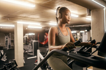 Fototapeta na wymiar A fit black sportswoman with headphones doing workouts on stair climbing machine at gym