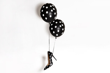 Fashionable shoe with a high heel with polka dots hangs on black and white polka dot balloons....