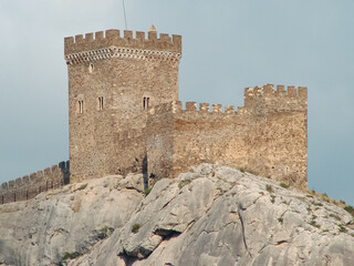 A fortress in the Romanesque style of the time of the knights, which stands on the edge of a stone cliff. Architectural building of the Middle Ages against the background of rocky nature.