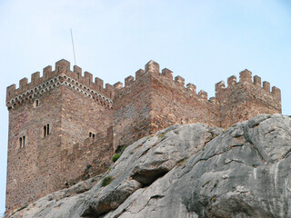 A fortress in the Romanesque style of the time of the knights, which stands on the edge of a stone cliff. Architectural building of the Middle Ages against the background of rocky nature.