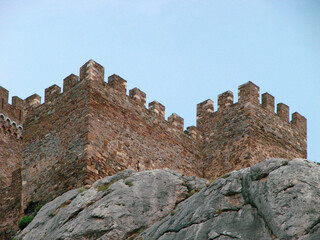 Fototapeta na wymiar A fortress in the Romanesque style of the time of the knights, which stands on the edge of a stone cliff. Architectural building of the Middle Ages against the background of rocky nature.