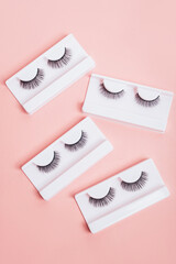 Different fake eyelashes in boxes on trendy pastel pink background. Makeup accessories. cosmetics products for women. Top view, flat lay. Layout. Place for text and design.