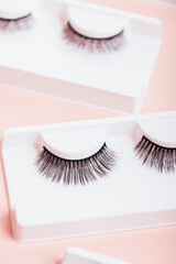 Different fake eyelashes in boxes on trendy pastel pink background. Makeup accessories and beauty cosmetics products for women. Top view, flat lay.