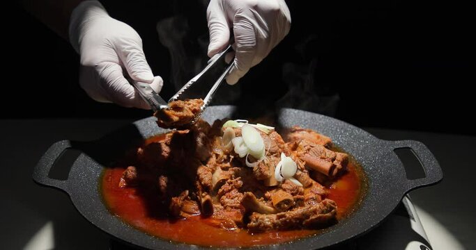 그리들에 매운 양념 돼지갈비를 구우며 가위로 뼈를 발라내는 