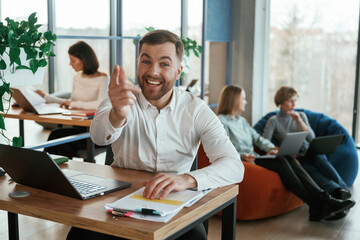 Happy man is smiling, sitting by table. People are working in the office with bean bags chairs in it