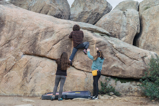 Anonymous Climbers work together on a complex boulder problem, with two spotting while one ascends the rock face