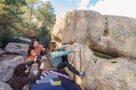 A climber is assisted by friends while navigating a tricky section of a boulder in a beautiful forest setting