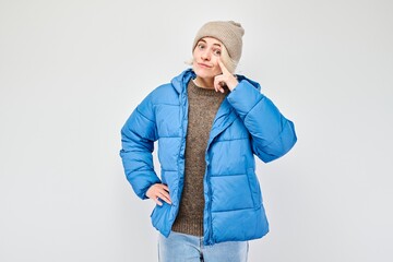 Woman in blue puffer jacket and beanie gesturing a call me sign against a light background.
