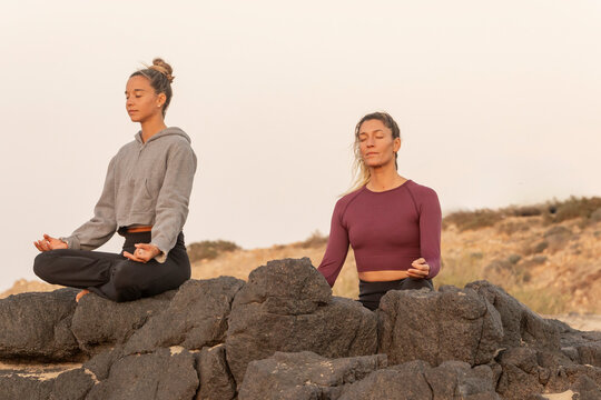 Serene female yoga practitioners meditating on a beach at sunset