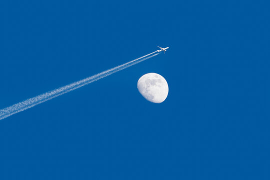 Airplane flying by the moon with clear blue sky