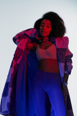 sexy african american woman in bra and faux fur looking at camera surrounded by red and blue lights