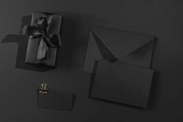 Black gift box with satin ribbons and a black envelope on a black background and label. Greeting card, certificate.