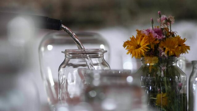 Wasser wird langsam in eine Karaffe gegossen, Blumen im Hintergrund