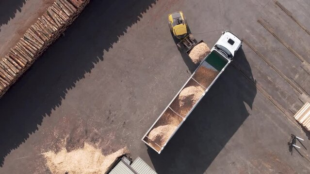 Drone shot of a payloader loading bulk of sawdust into trailer truck at wood factory on a sunny day