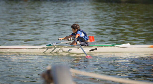 10 year old boy training rowing in a lake near his home with blue life jacket on a summer afternoon.