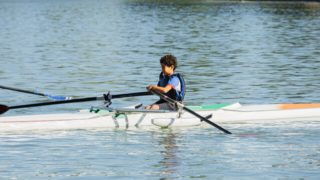 Boy training rowing in a lake near his home with blue lifejacket
