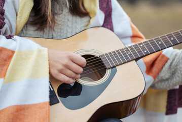 Close up of a girl playing guitar outdoors. Young girl covered in warm plaid playing acoustic...