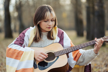 Portrait of a young girl playing the guitar outdoors. Beautiful girl playing the guitar in autumn...