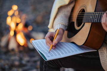 Girl composer playing the guitar composing new song outdoors near bonfire. Playing the guitar in...