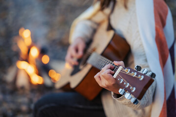 Close up of a girl playing the guitar near bonfire. Playing the guitar outdoors on nature, having...