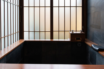 Hot spring zen inspired for Japanese bathroom featuring a stone bath, wooden accents and morning light through shoji screen