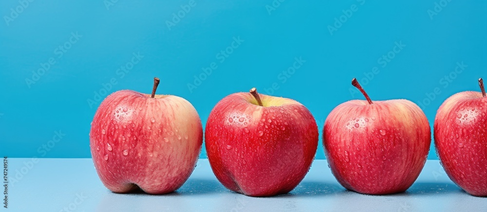 Canvas Prints A row of vibrant red Starking apples neatly lined up on top of a wooden table. The apples are shining under the light, showcasing their rich color.