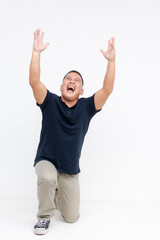 A euphoric middle-aged Asian man in casual attire kneeling and shouting in joy with arms up,...