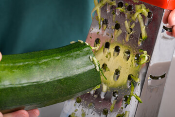 grating green zucchini with a stainless steel hand grater, close up, food lifestyle, vegan and vegetarian recipe, preparing food