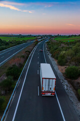 Refrigerator truck driving on a highway that disappears into the horizon at sunset, elevated view.