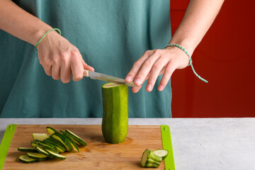 Authentic female hands cutting zucchini on wooden cutting board on kitchen table. Woman in apron cut zucchini for preparing food. Vegan and vegetarian recipe, cuisine. Domestic life, lifestyle