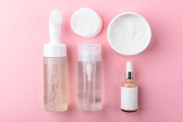 Facial cotton pads, foam, tonic, serum and cream on pink background. Facial skin care.