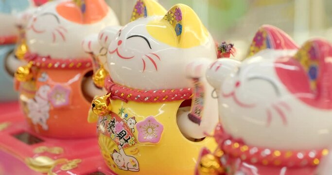 Maneki-neko, cat with a paw raised in a beckoning gesture, common Japanese figurine which is bring good luck to the owner. Close-up handheld real-time shot in artificial indoors light.
