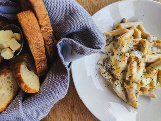 Meal in the restaurant. fresh and delicious penne pasta sprinkled with parmesan and spices. next to it is a napkin and a basket of fragrant freshly baked bread. Food is on the wooden table
