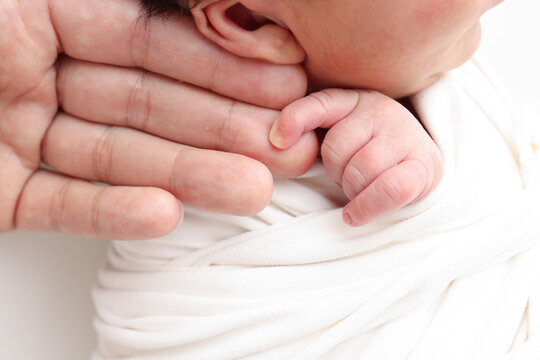 Close-up of baby's small hand, head, ear and palm of mother. Macro Photo of Newborn baby after birth tightly holding parents finger on white background. Family and home concept. Healthcare paediatrics