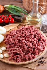 Raw minced meat in bowl on wooden table and ingredients. Ground meat with ingredients for cooking on wooden table.