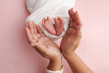 The palms of the father, the mother are holding the foot of the newborn baby in a white blanket, pink background. Feet of the newborn on the palms of the parents. photo child's toes, heels and feet.