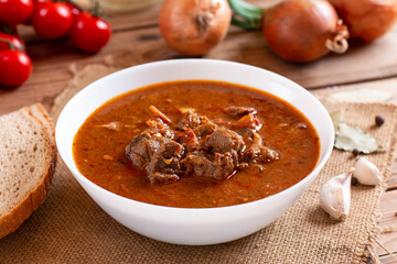 Pork goulash meat on plate, cutlery, garlic, onion, in the background - typical Czech food