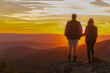 two silhouettes of two tourists in love against the background of an evening sunset in the mountains