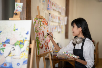 A smiling young woman enjoys painting a colorful canvas in a cozy, homey art studio.